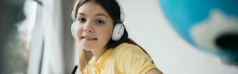 smiling girl looking at camera while listening music in headphones, banner