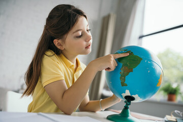 preteen schoolgirl pointing at globe while learning geography at home