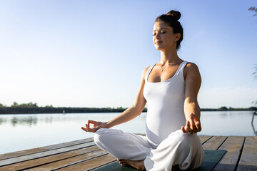 Fototapeta na wymiar Pregnant woman doing yoga at lake during the day.