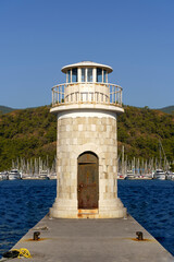 Lighthouse tower on the shore of the seaport. Ancient decorative lighthouse on the pier. Marine buildings concept.
