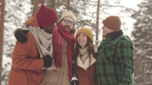 Portrait of cheerful diverse company of friends smiling at camera standing in snowy winter forest