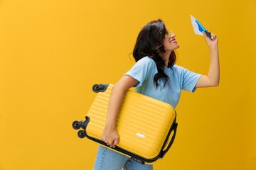 Traveler woman with yellow suitcase, passport and ticket in hand, paper plane, blue t-shirt and jeans on yellow background tourist, travel happiness, glasses, copy space