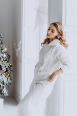 Young happy blonde woman in white clothes on the background of a Christmas tree. Soft selective focus.
