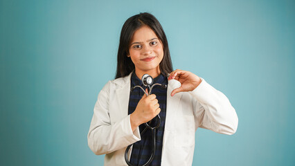 Portrait of a young female doctor cardiologist showing heart symbol with fingers, Cheerful Asian Indian woman doctor in apron and stethoscope isolated blue studio background, expressing love and care
