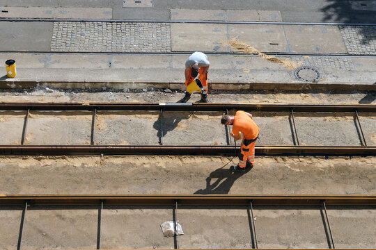 Konzept Infrastruktur Sanierung und Ausbau: Zwei Arbeiter in Arbeitskleidung erneuern und reparieren die Schienen und das Gleisbett einer Stra&szlig;enbahnstrecke in einer Stadt, Luftaufnahme