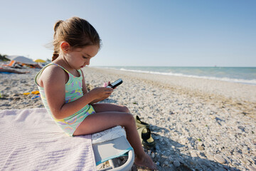 Baby girl sitting and play phone at sea beach Porto Sant Elpidio, Italy.