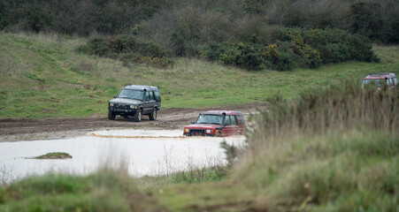 Plakat three land rover discovery 4x4 off-road vehicles being driven through deep water and mud in open countryside, Wiltshire UK