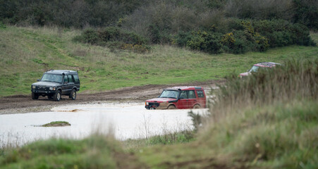 Obraz na płótnie Canvas three land rover discovery 4x4 off-road vehicles being driven through deep water and mud in open countryside, Wiltshire UK