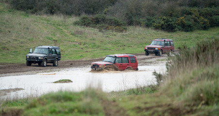 Obraz na płótnie Canvas three land rover discovery 4x4 off-road vehicles being driven through deep water and mud in open countryside, Wiltshire UK