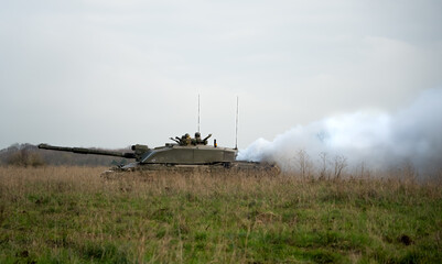 Fototapeta premium commander and gunner directing action on a British army FV4034 Challenger 2 ii main battle tank, diesel smoke screen billowing from the rear on a military exercise, Wiltshire UK