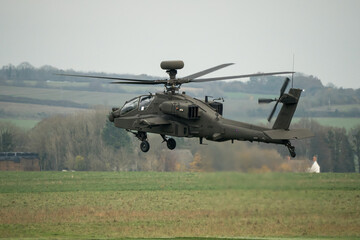 close up side view of British army Boeing Apache Attack helicopter AH-64E (ZM722 ArmyAir606) landing in a meadow, autumn sky