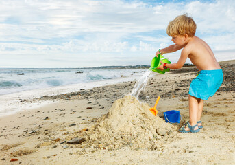 Boy play with sand pouring water from plastic bucket side view