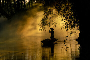 Photo of a local asian old man male boatman wearing conical hat rowing a small wooden boat across a...