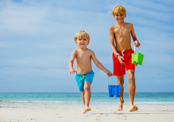 Fototapeta premium Two happy smiling boys run with water buckets from sea waves