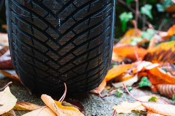 Close up of brand new all weather car tire on wet asphalt covered in yellow autumn season leaves....
