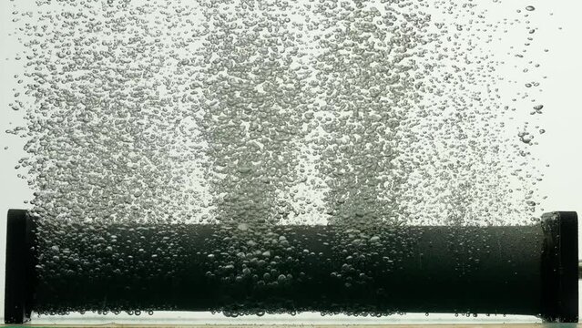 Stream of air bubbles escaping from dark paralon tube of compressor or filter underwater in aquarium. Close up of rising oxygen bubbles in liquid on white isolated background. Slow motion.