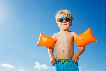 Boy in inflatable shoulder straps stand on the over sky at beach