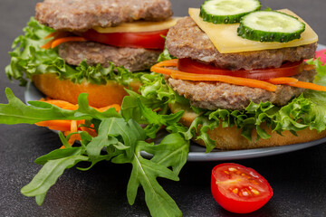 Cheeseburgers with cucumber, greens, chopped onions and carrots on gray plate.