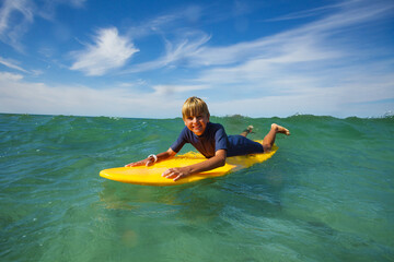 Happy boy lay on surf board smiling and looking at camera