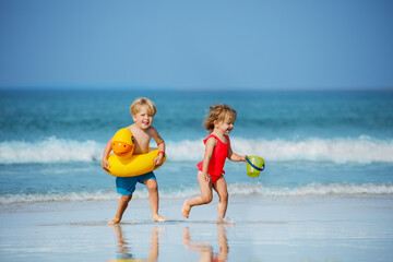Naklejka premium Boy with girl run holding inflatable buoys duck and toy at beach