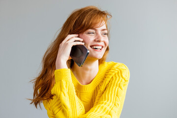 Young red-haired smiling woman sitting with mobile phone. Young red-haired woman holding mobile phone. Friendly cheerful young redhead woman