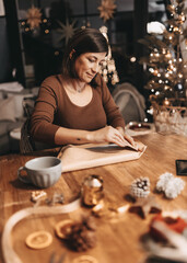 Good mood woman in a cozy environment wrapping gifts for Christmas, stylish decoration, vintage, warm colors