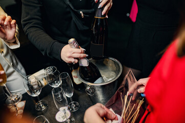 Bachelorette party and table with alcohol, champagne bottles, glasses and female hands. Open a bottle of booze. Holiday