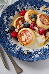 Homemade cottage cheese pancakes with sour cream and blueberries and raspberries and almond leaves in a vintage blue plate