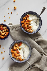 Blue bowls with greek yogurt with almond, coconut and cashew granola on marble table with linen grey tablecloth top view