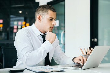 Young businessman working at office with laptop and documents on desk.