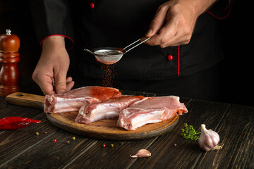 Chef adds paprika to raw meat ribs before grilling. Work environment on the kitchen table with spices and condiments
