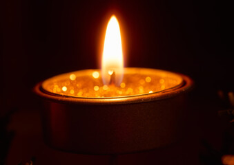 lit small candle, with gold glitter, with defocused dark background and orange bokeh