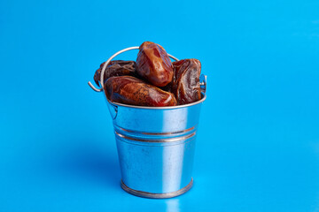 A small metal bucket filled with dried dates on a blue background.