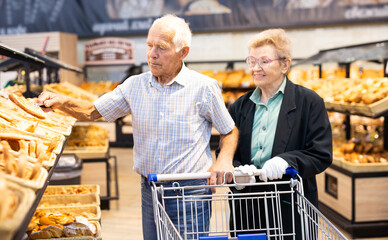 mature european couple shopping buns and bread in bakery section of supermarket