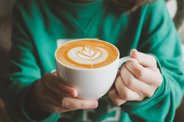Beautiful girl in green sweater holding cup of tea or coffee in the morning. Closeup of female hands holding a mug of beverage.