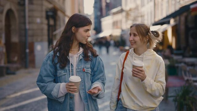 Two lesbian women walking on the street holding, drinking coffee, talking and laughing. Lgbt couple feeling in love, spending time together. Woman relationships, lgbt concept
