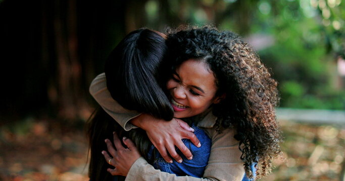 Two enthusiastic women embrace outside at park, happy friends reunion