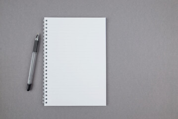 white notebook with a pen on a gray background, top view.