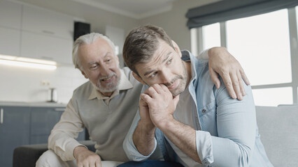 Wise senior father comforting sad son at home, giving advice, family support