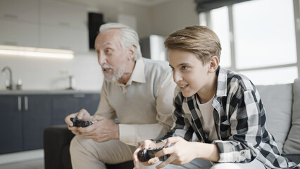 Excited pensioner and grandson playing video game together at home, family