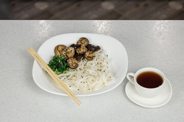 Plate with rice noodles and shiitake mushrooms. White mug with coffee