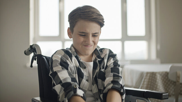 Teenager in wheelchair feeling acute knee pain, rehabilitation after injury, disability
