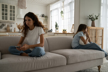 Fototapeta premium Emotionally exhausted mother of difficult teenager thinking about conflict with daughter, holding smartphone looking for psychologist for teen child. Family misunderstanding, parent-child relationship