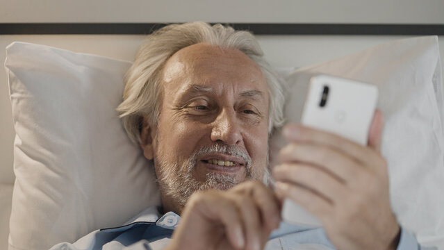 Smiling senior man using smartphone in bed, communication online, dating app