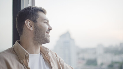 Happy handsome man smiling, looking out the window, enjoying view, urban scenery