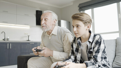 Active grandpa playing video game with his teenage grandson, having fun together