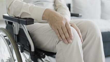 Close-up of man in wheelchair rubbing injured knee, rehabilitation after injury, arthritis