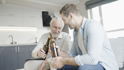 Happy senior father and young son clinking beer bottles and smiling, celebration