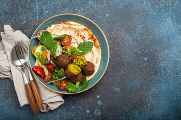 Middle Eastern Arab meal with fried falafel, hummus, vegetables salad with fresh green cilantro and mint leaves in ceramic bowl on stone rustic background top view. Arabic cuisine, space for text