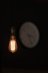 Vertical photo of classic vintage Edison light bulb and white clock on black background with space...